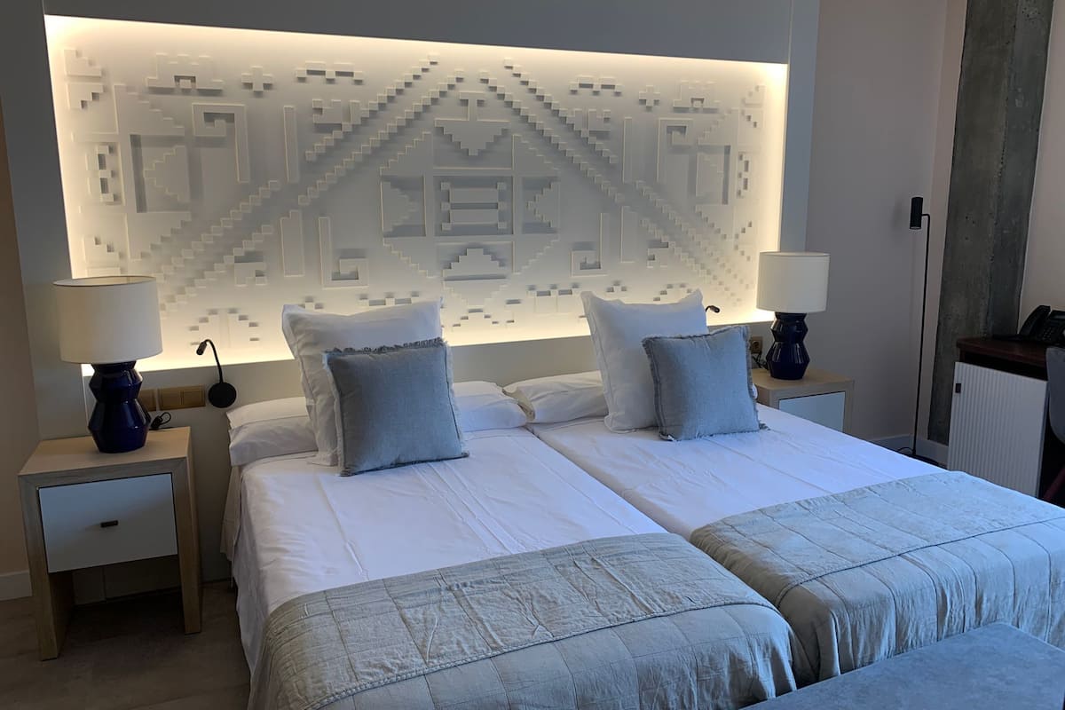 Quarto de hotel moderno com uma cama grande, duas mesas de cabeceira e um design de parede geométrico exclusivo.