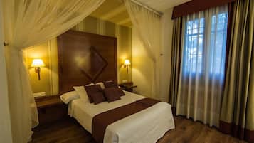 Una habitación de hotel con una cama grande, dos lámparas de noche, un cabecero de madera y cortinas de encaje.