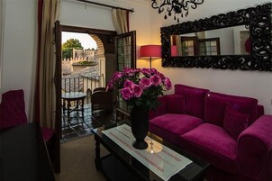 Una habitación con un sofá rojo, una mesa con un florero, un espejo y vistas a un patio.