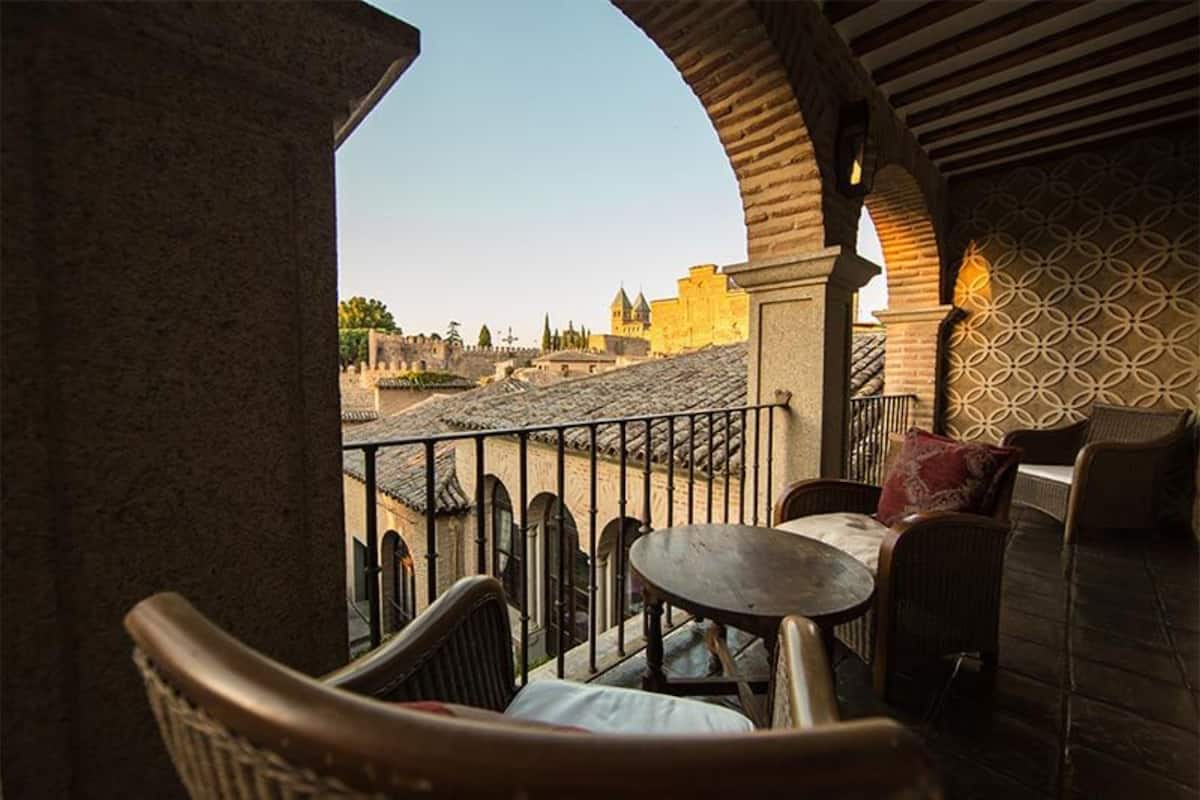 Varanda com cadeiras de vime e uma mesa, com vista para um centro hist órico e arquitetura marcante.