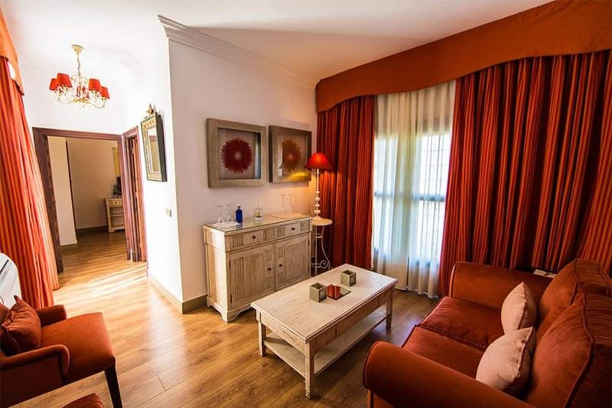 Uma sala de estar com piso de madeira, um sofá, uma mesa de centro, um aparador e um lustre.