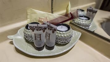 Un tocador de baño con espejo, lavamanos y artículos de aseo personal, incluyendo un peine, dos productos para el cabello y una vela.