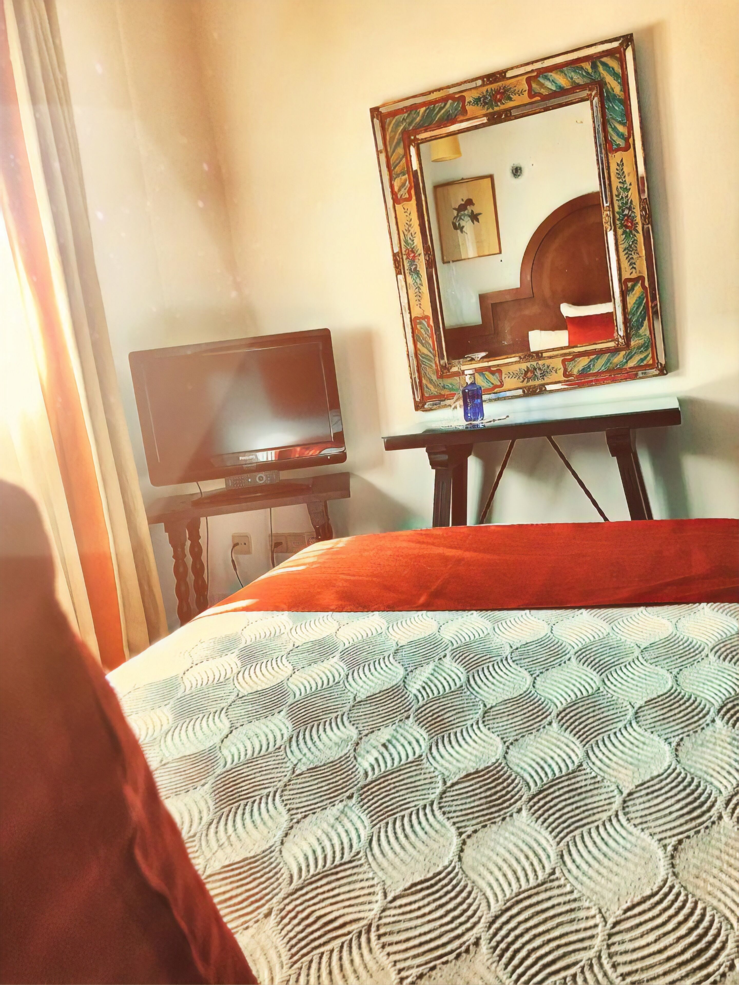 A hotel room with a bed, a television, a mirror, and a small table.