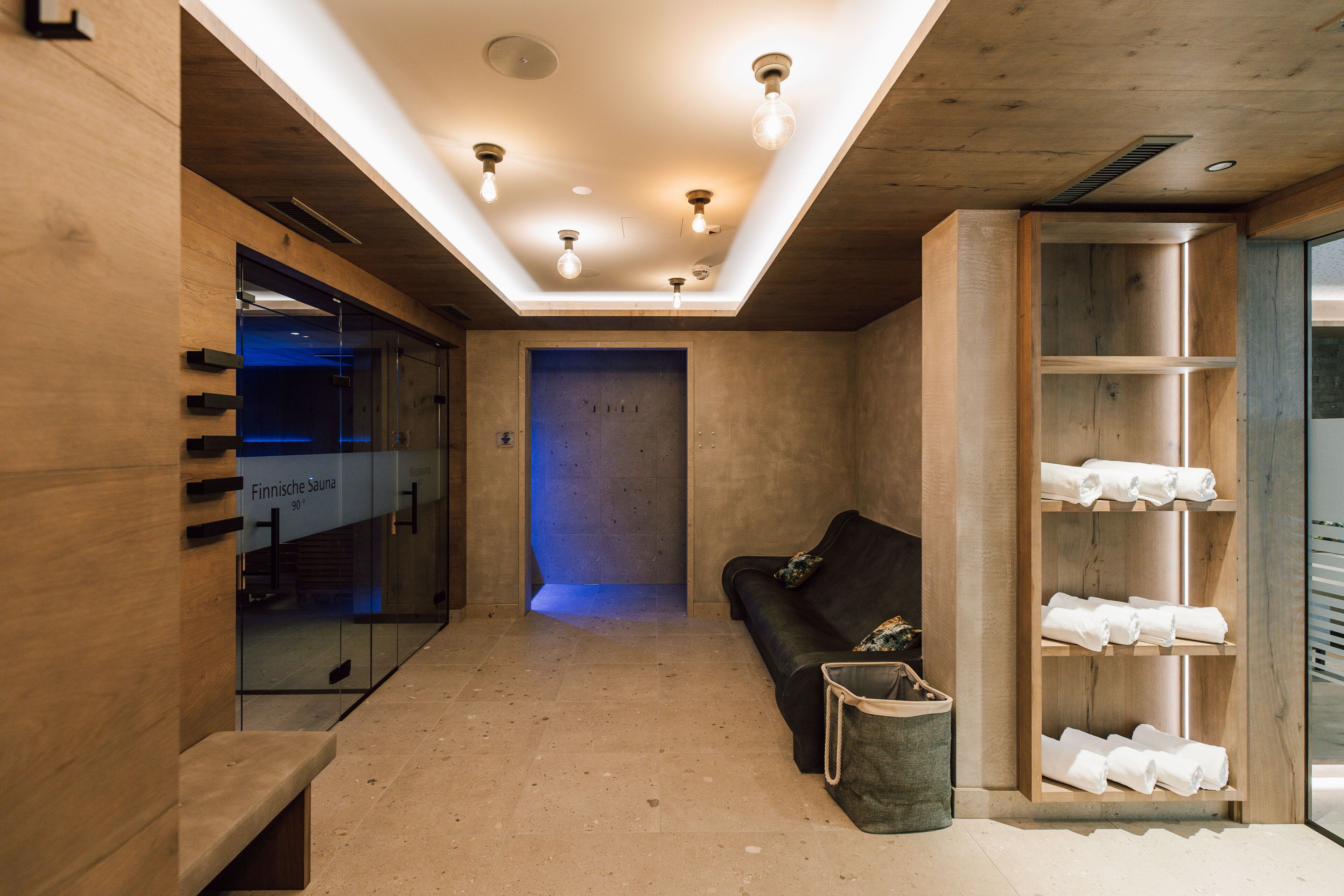 A sauna room with wooden walls, a bench, a glass door, and a shelf with towels.