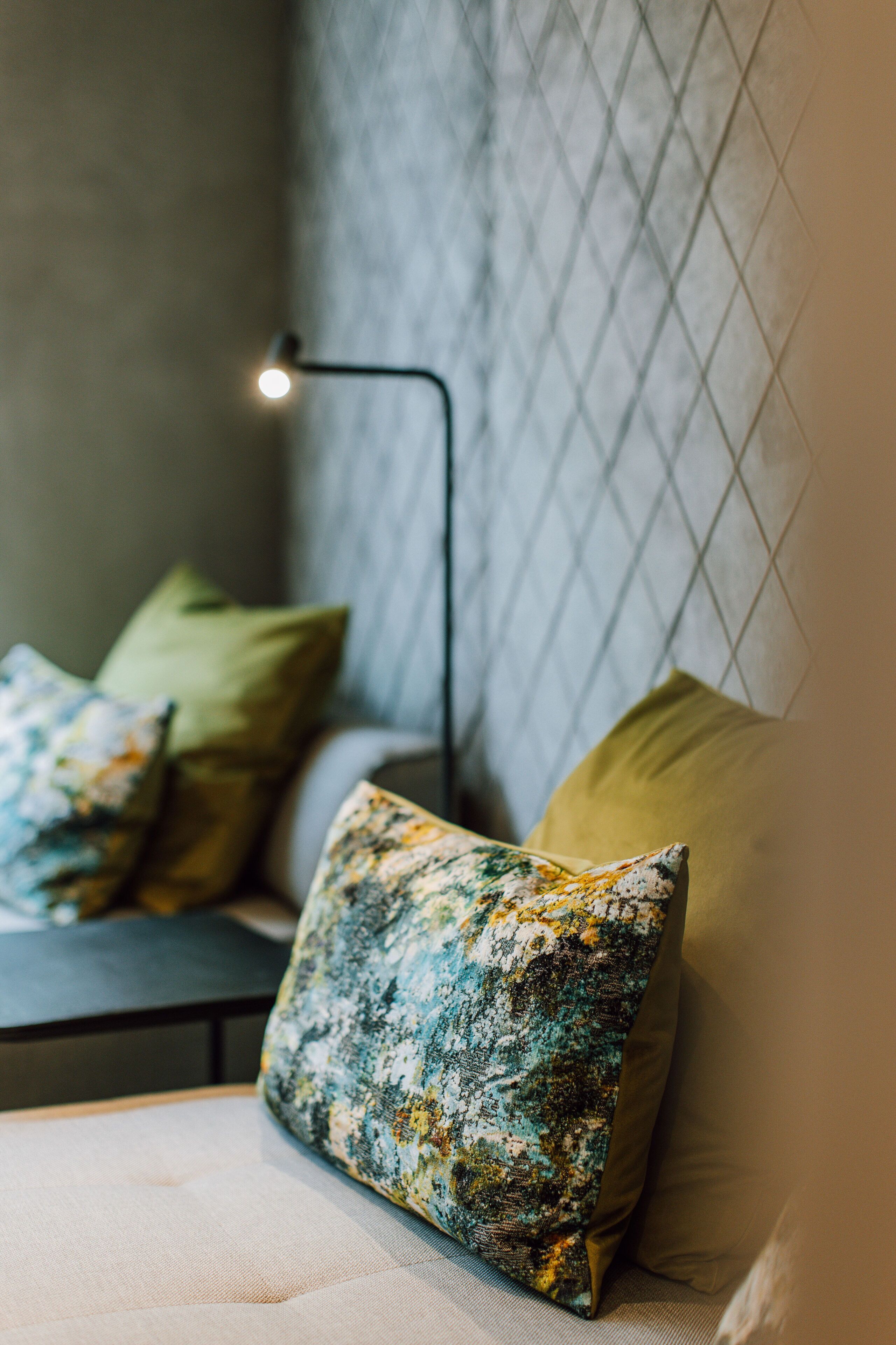 Un coin salon confortable avec un banc rembourré, un coussin à motifs et une lampe fixée au mur.