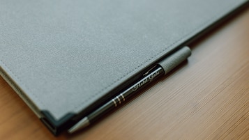 A closed laptop with a pen inserted into its side.