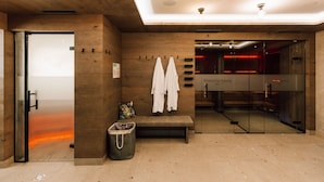 Zona de sauna con paredes de madera, un banco y toallas colgadas de ganchos.