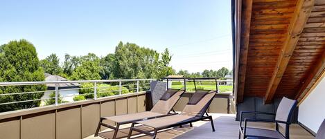 A balcony with two sun loungers and a table, overlooking a green landscape.