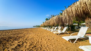 A sandy beach with white lounge chairs and a thatched umbrella. - Summery Hotel (Kefalonia)