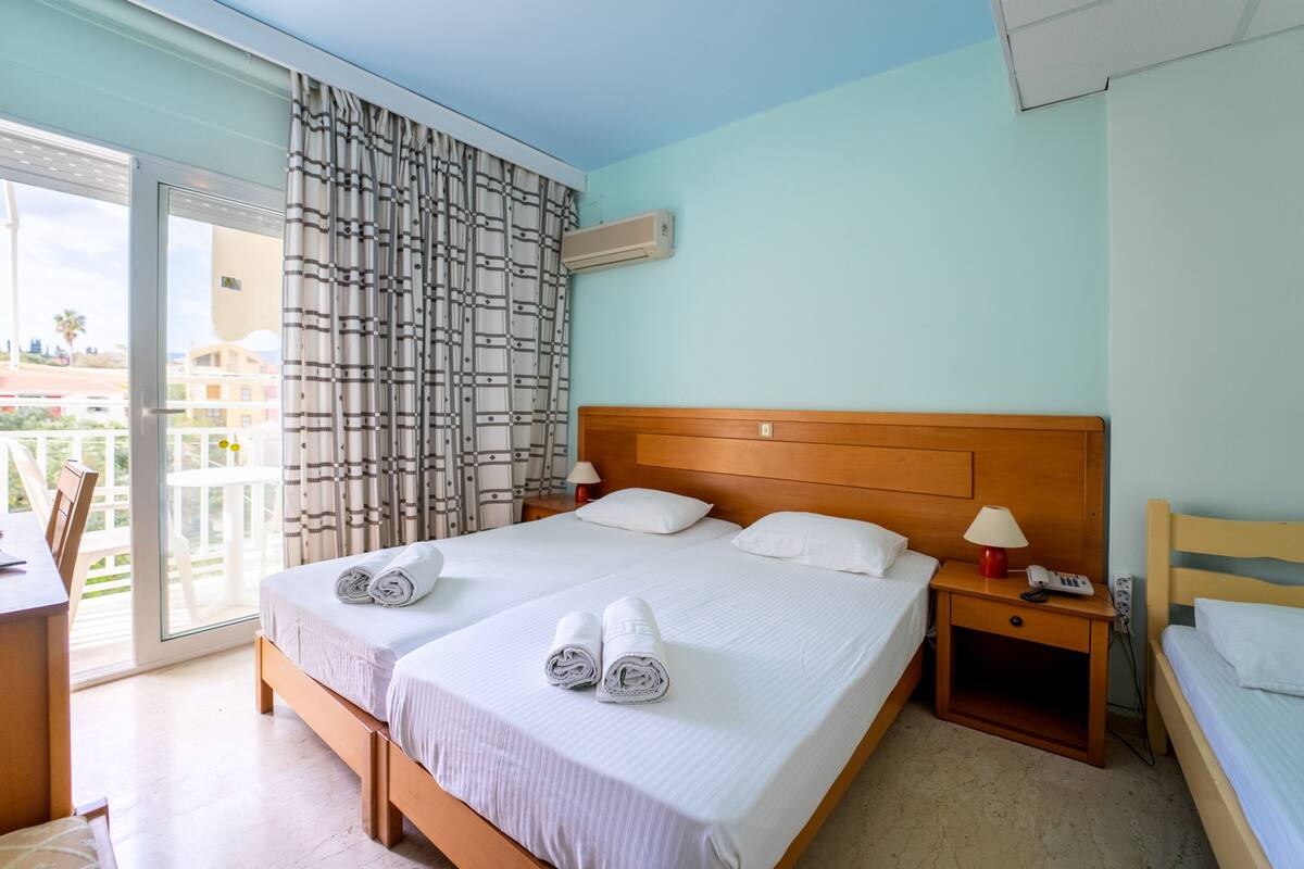 A hotel room with a large bed, two bedside tables, a desk, and a balcony with a view of buildings.