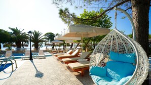 A pool area with lounge chairs, a hanging chair, and umbrellas. - Summery Hotel (Kefalonia)