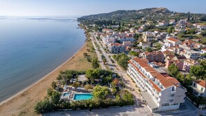 An aerial view of a coastal town with a beach, a swimming pool, and residential buildings. - Summery Hotel (Kefalonia)