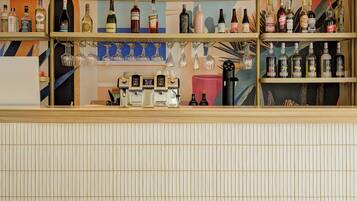 A bar area with shelves of bottles and glasses, a coffee machine, and a tiled floor.