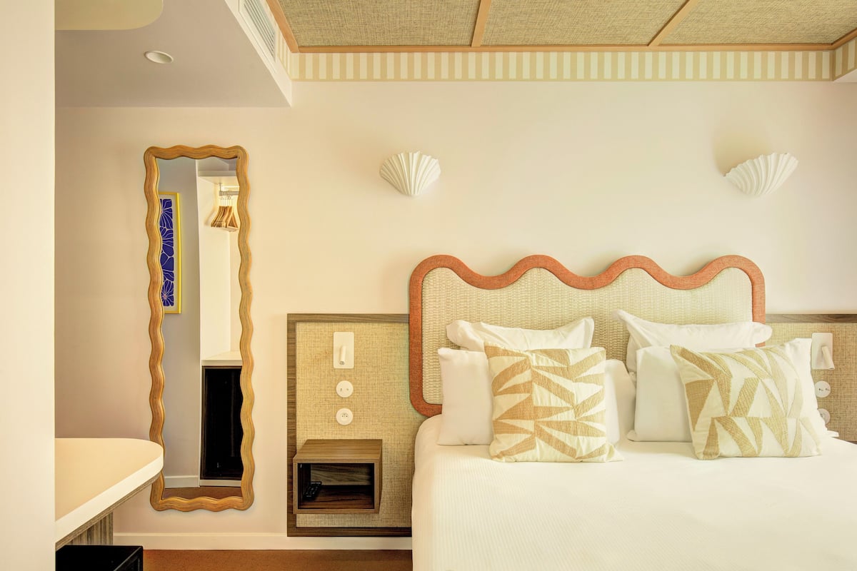 Una habitación de hotel con una cama grande, un espejo y una mesita de noche pequeña.