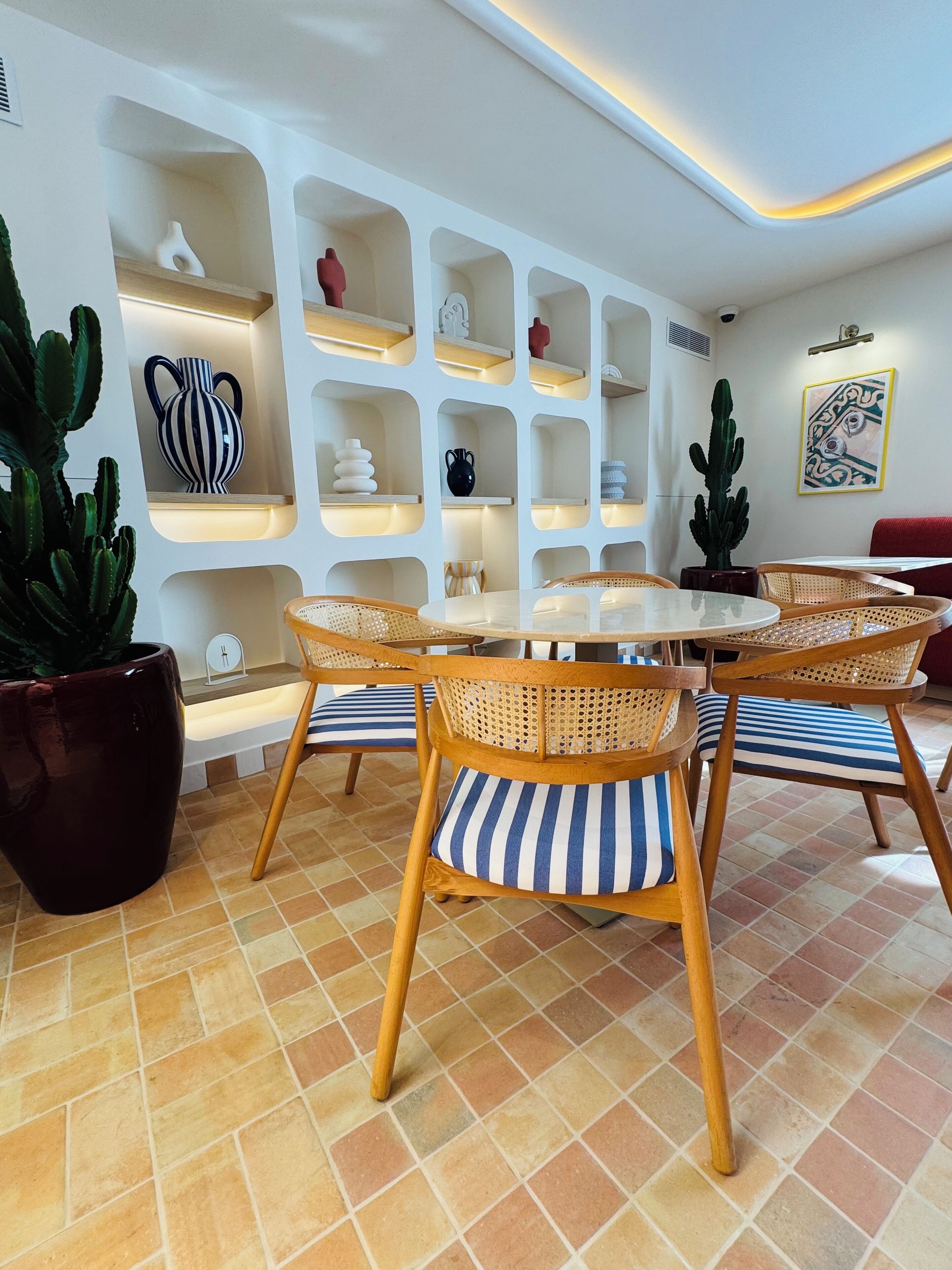 Un comedor con una mesa redonda y sillas de mimbre, rodeado de estanterías blancas con objetos decorativos.