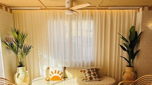 Una habitación acogedora con un sofá a rayas, dos sillones de mimbre, una mesa redonda de madera y un ventilador de techo.