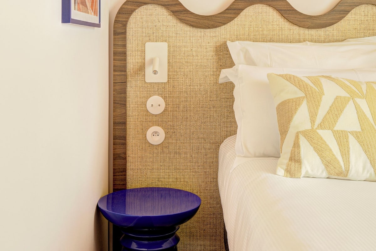 Habitación de hotel con cama, mesita de noche, lámpara de pared e imagen enmarco.