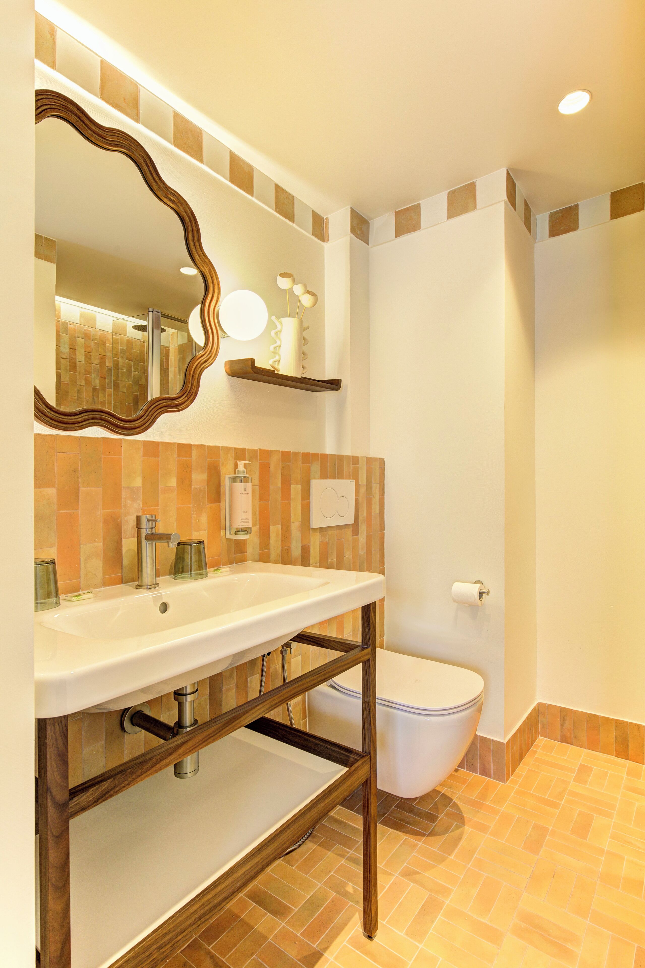 A bathroom with a white sink, a mirror with a wavy frame, a toilet, and a shower area.