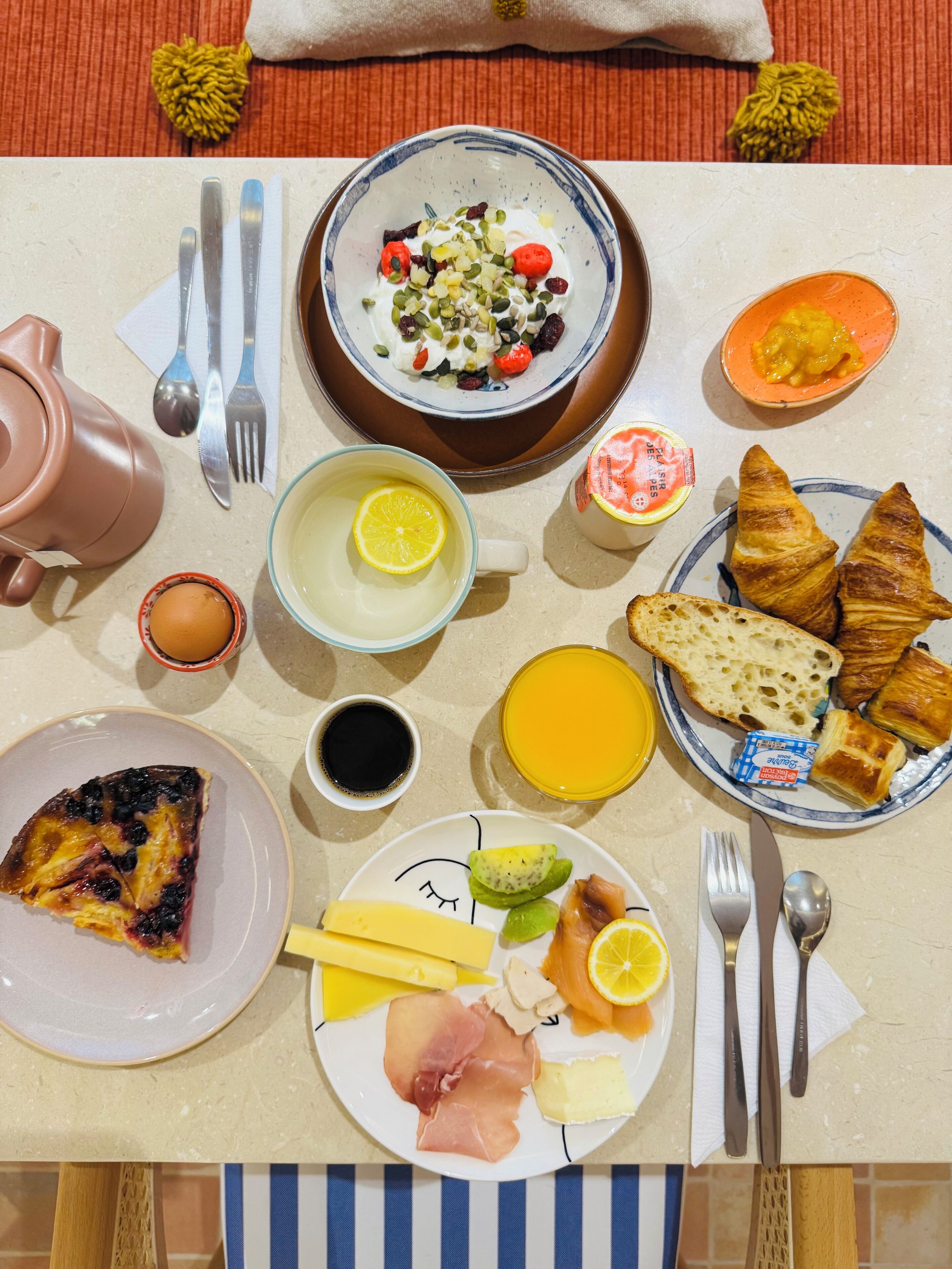 A breakfast table with various food items, including croissants, a slice of quiche, and a plate with ham and cheese.