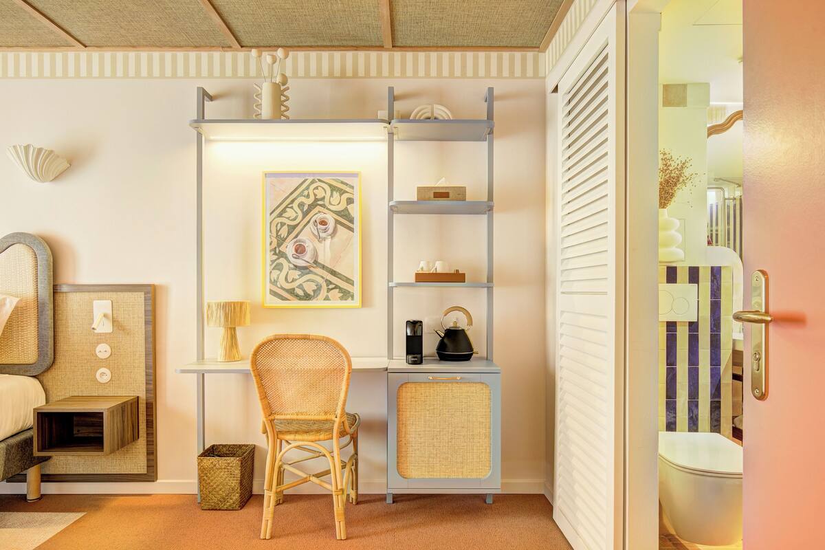 Una habitación compacta con una cama, un escritorio con estanterías, una silla y un mueble pequeño.
