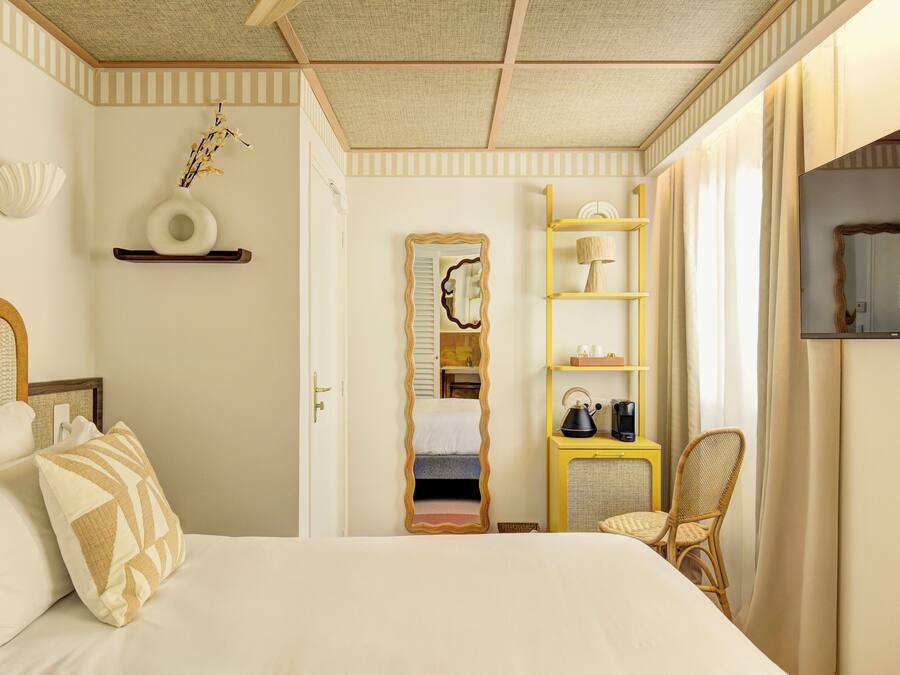 A bedroom with a bed, a chair, a shelf with toiletries, and a mirror.