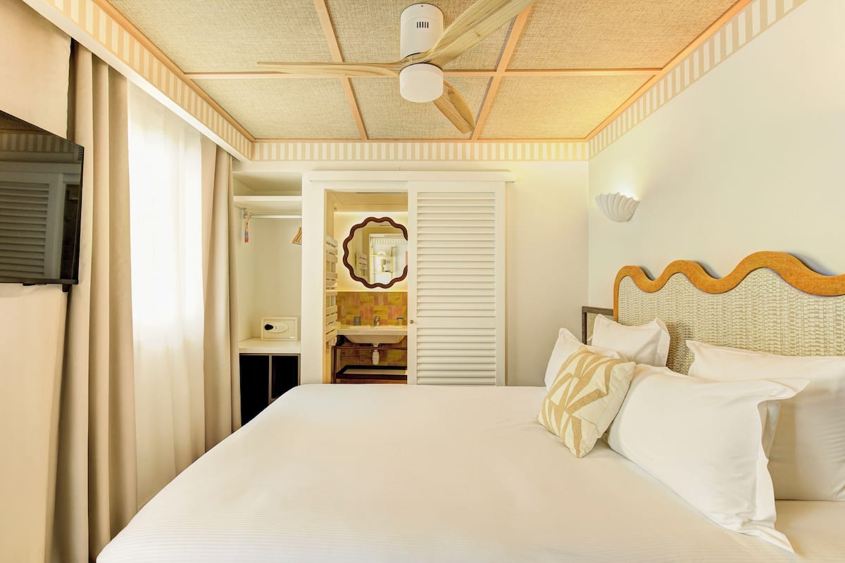 Una habitación de hotel con una cama grande, un ventilador de techo, un espejo y un armario.