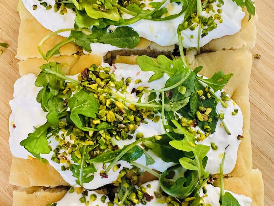 Una especie de pan plano cubierto de vegetales y salsa cremosa blanca.