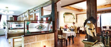 Interior de restaurante con pared de piedra, vigas de madera, una vitrina de vidrio y una estatua con forma de casco.