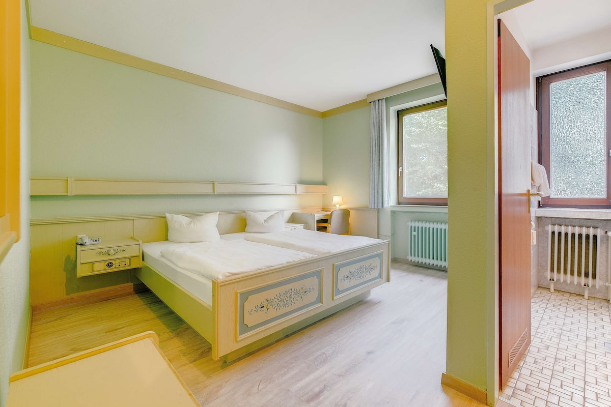 Une chambre à coucher avec un lit, une table de chevet, une lampe et une fenêtre donnant sur un beau paysage.