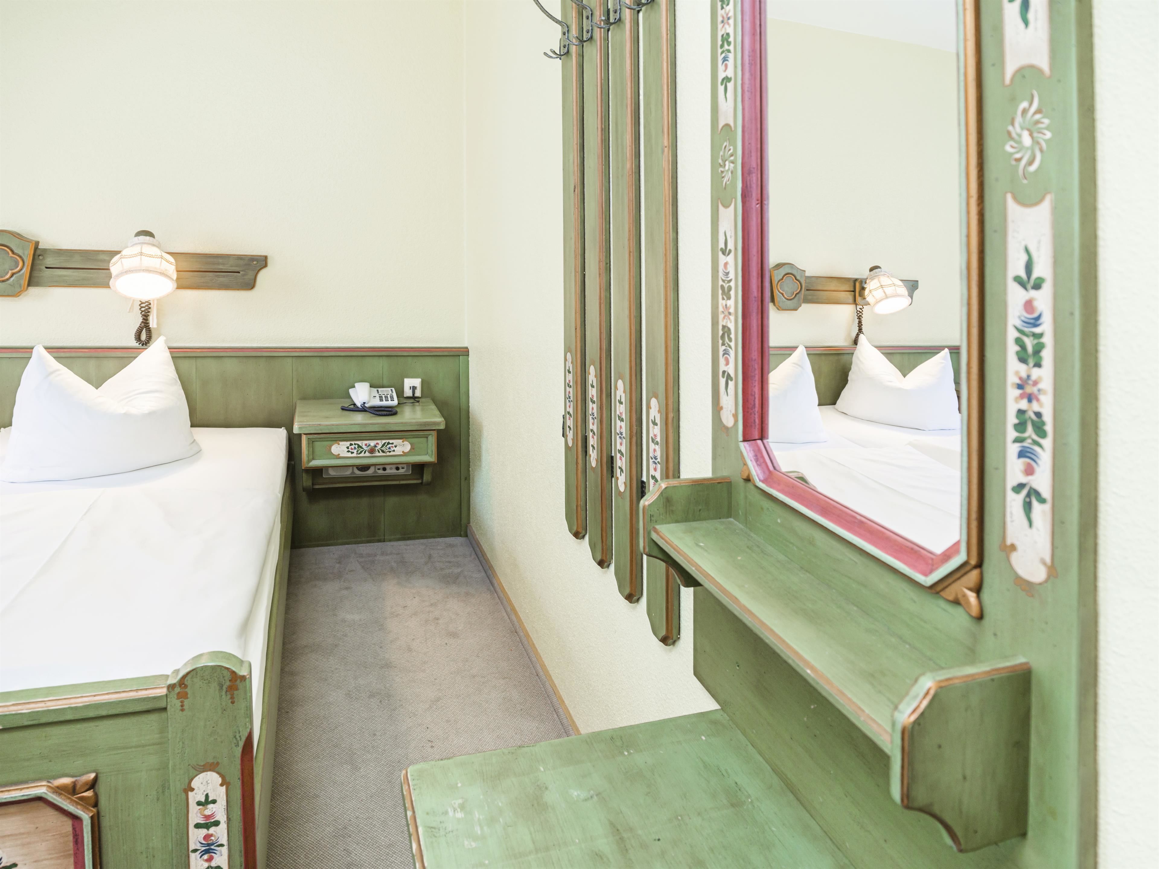 Een hotelkamer met een bed, nachtkastje, lamp, spiegel en een klein bureau met telefoon.