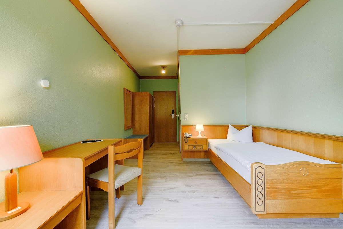 Une chambre d’hôtel avec un bureau, une chaise et un lit en bois, doté d’une tête de lit en bois.