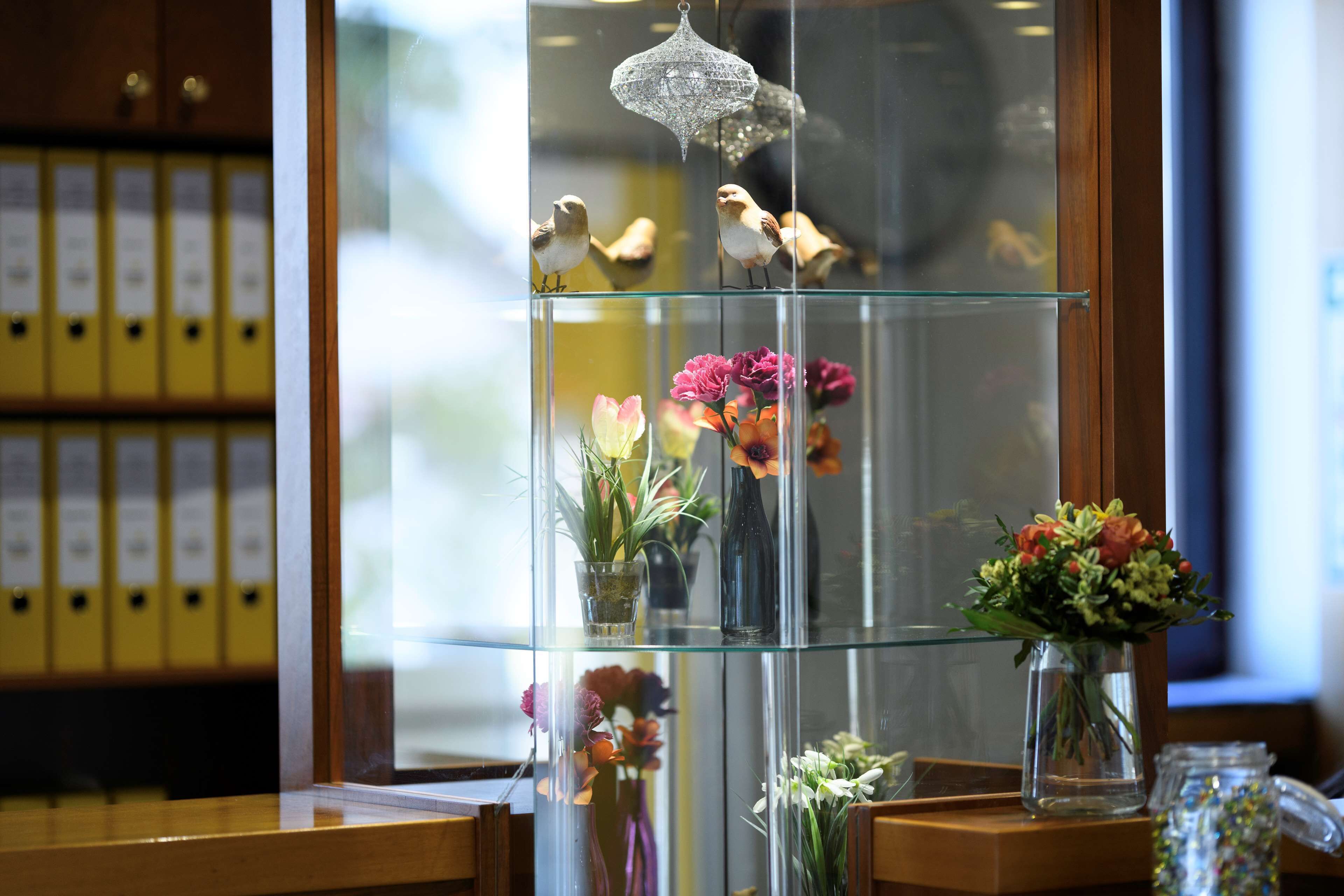 Un mostrador de recepción con una vitrina de vidrio que contiene flores y objetos decorativos.