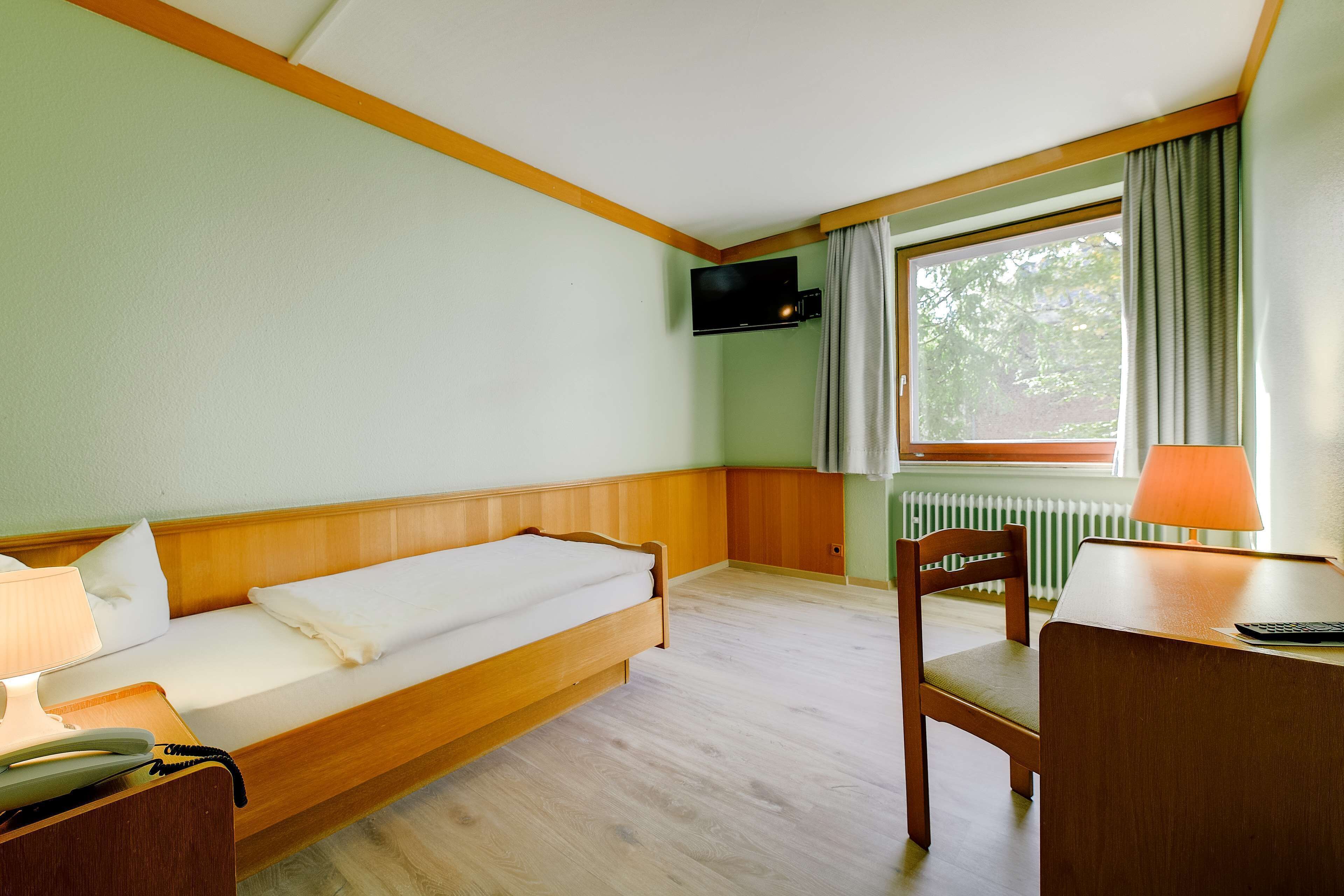 Una habitación con una cama, un escritorio, una silla, una lámpara, un teléfono y una televisión.