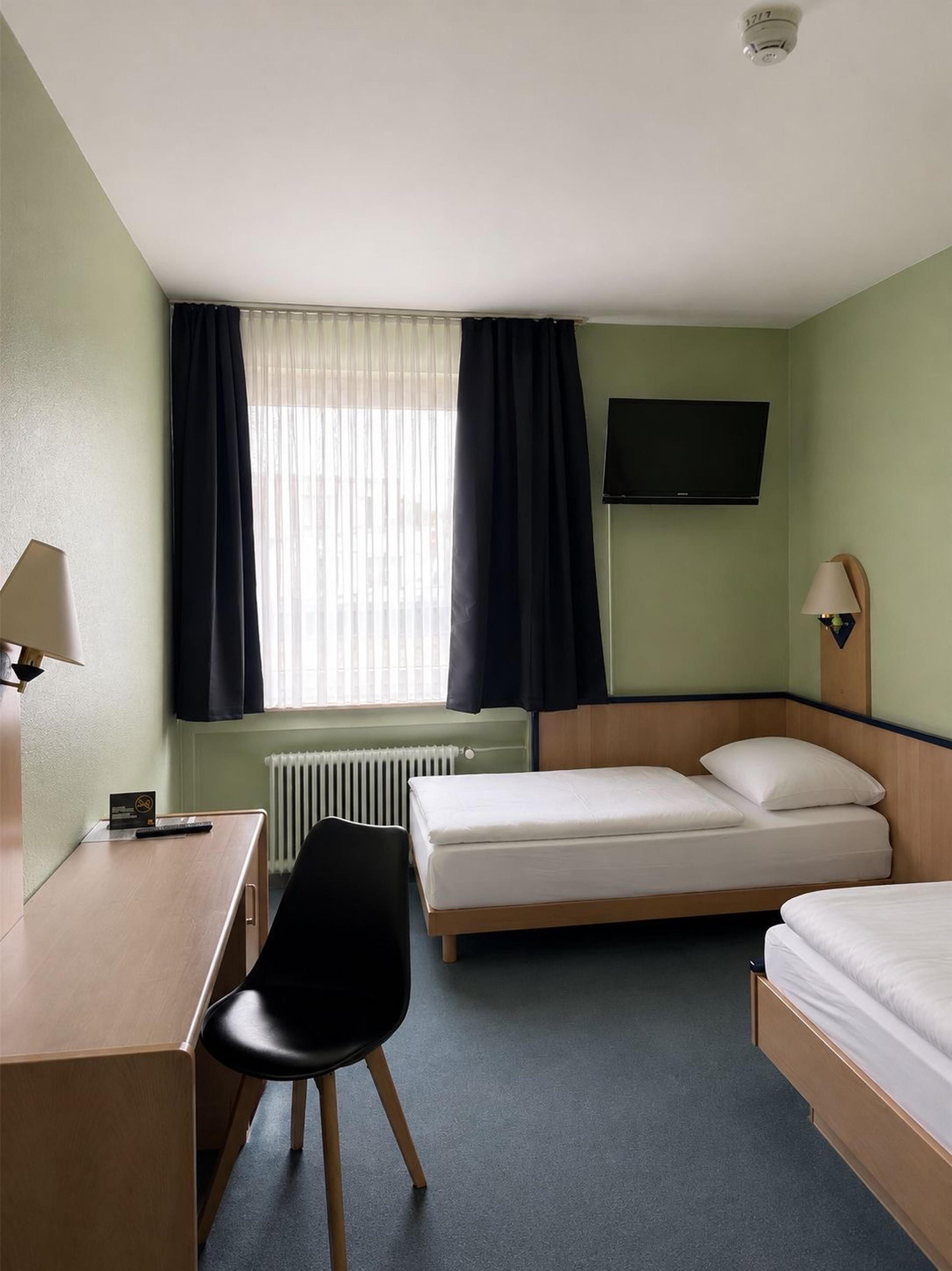 A hotel room with a bed, a desk, a chair, a television, and a window with curtains.