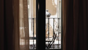 Vista por una ventana con baranda de balcón, una silla y una mesa.