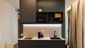 Cocina compacta con microondas, tetera y cafetera, un lavamanos pequeño y un armario con cristalería.