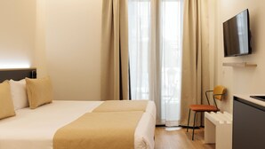Habitación de hotel con cama, escritorio, silla, televisor y ventana con cortinas.