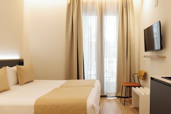A hotel room with a bed, a desk, a chair, a television, and a window with curtains.