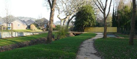 Un sendero atraviesa un parque con árboles y un pequeño puente sobre el agua.
