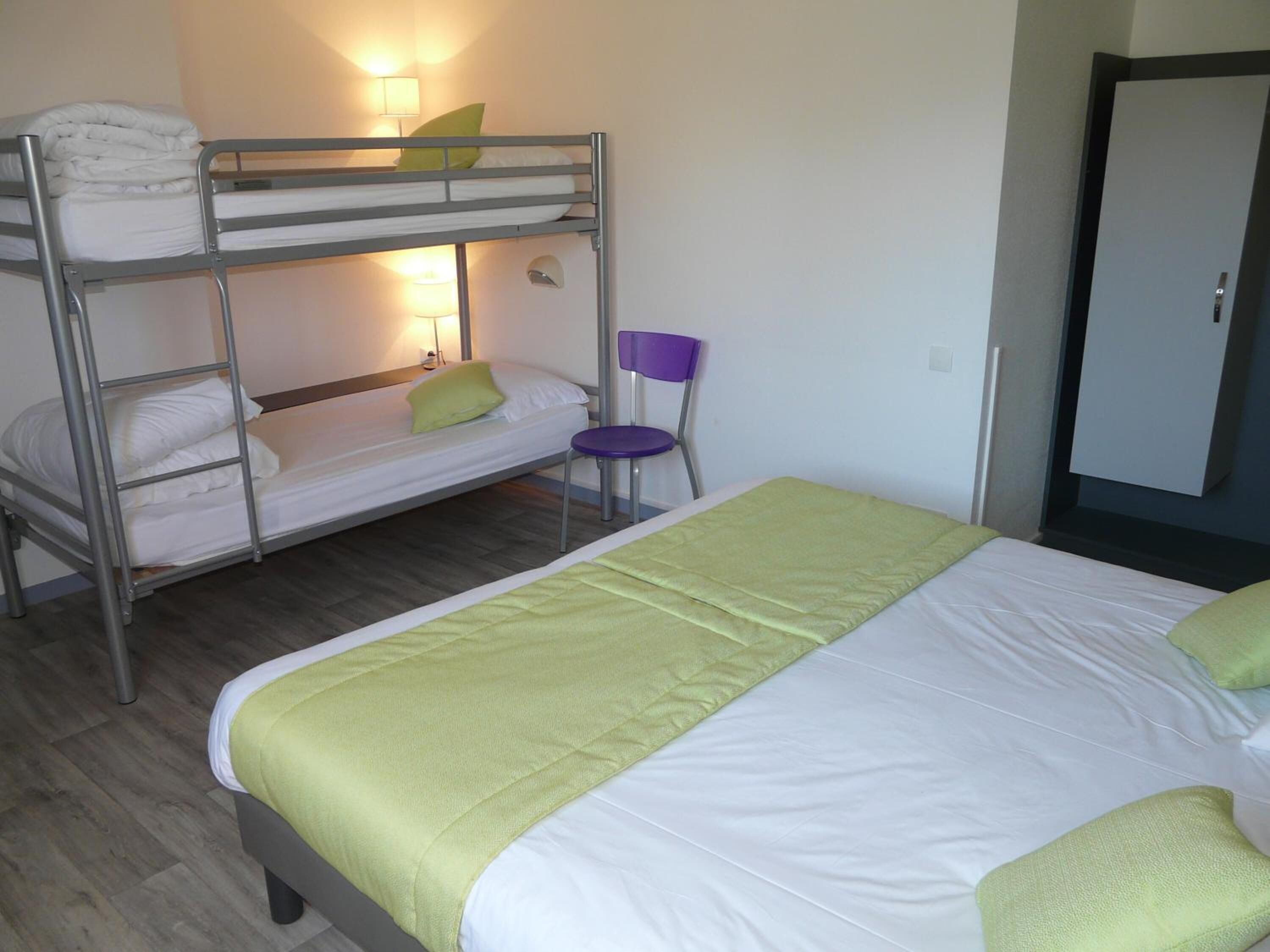 A room with bunk beds, a single bed, a chair, and a wardrobe.