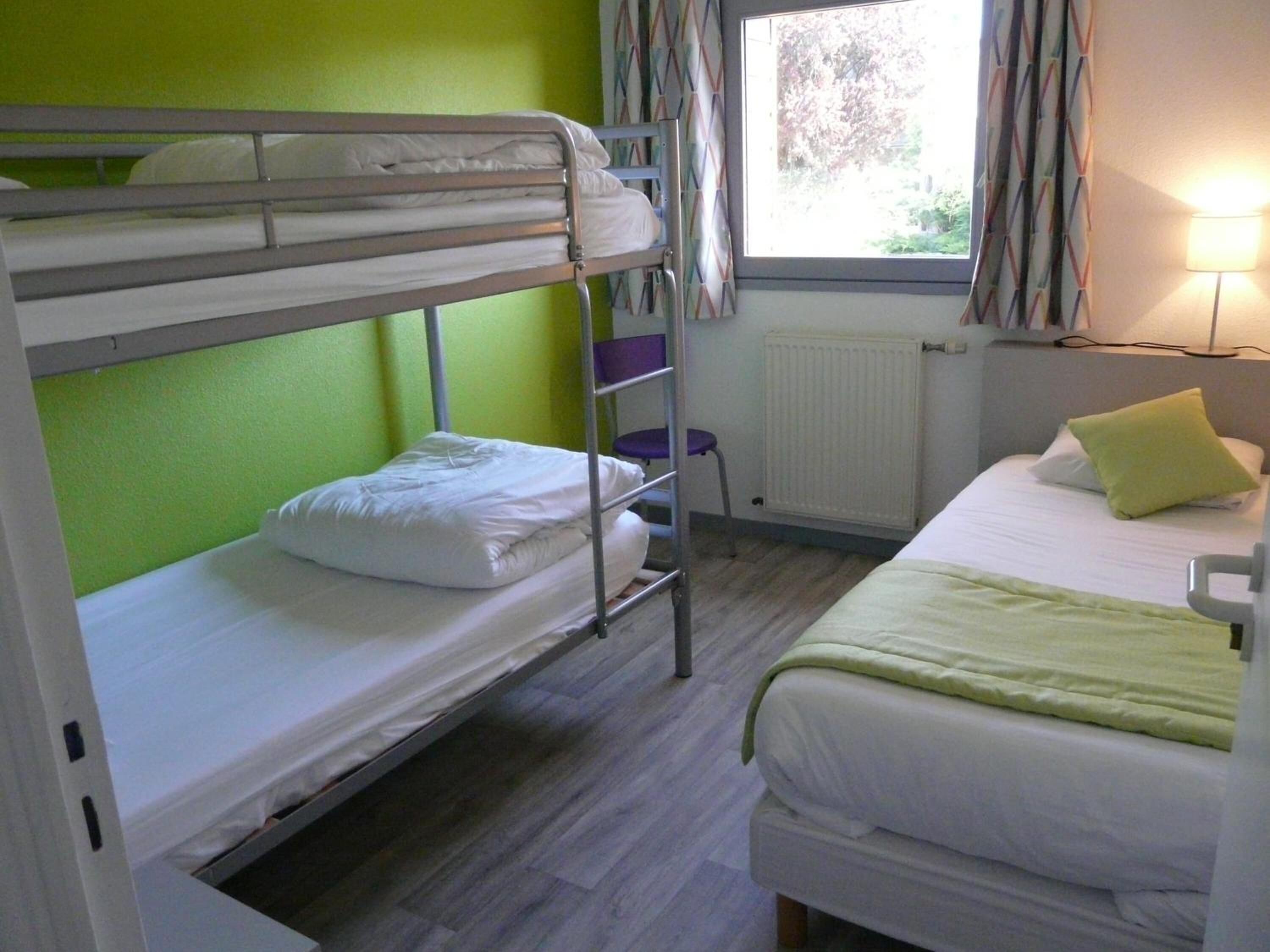 Un dormitorio con literas, una ventana con cortinas, un radiador y una lámpara de noche.