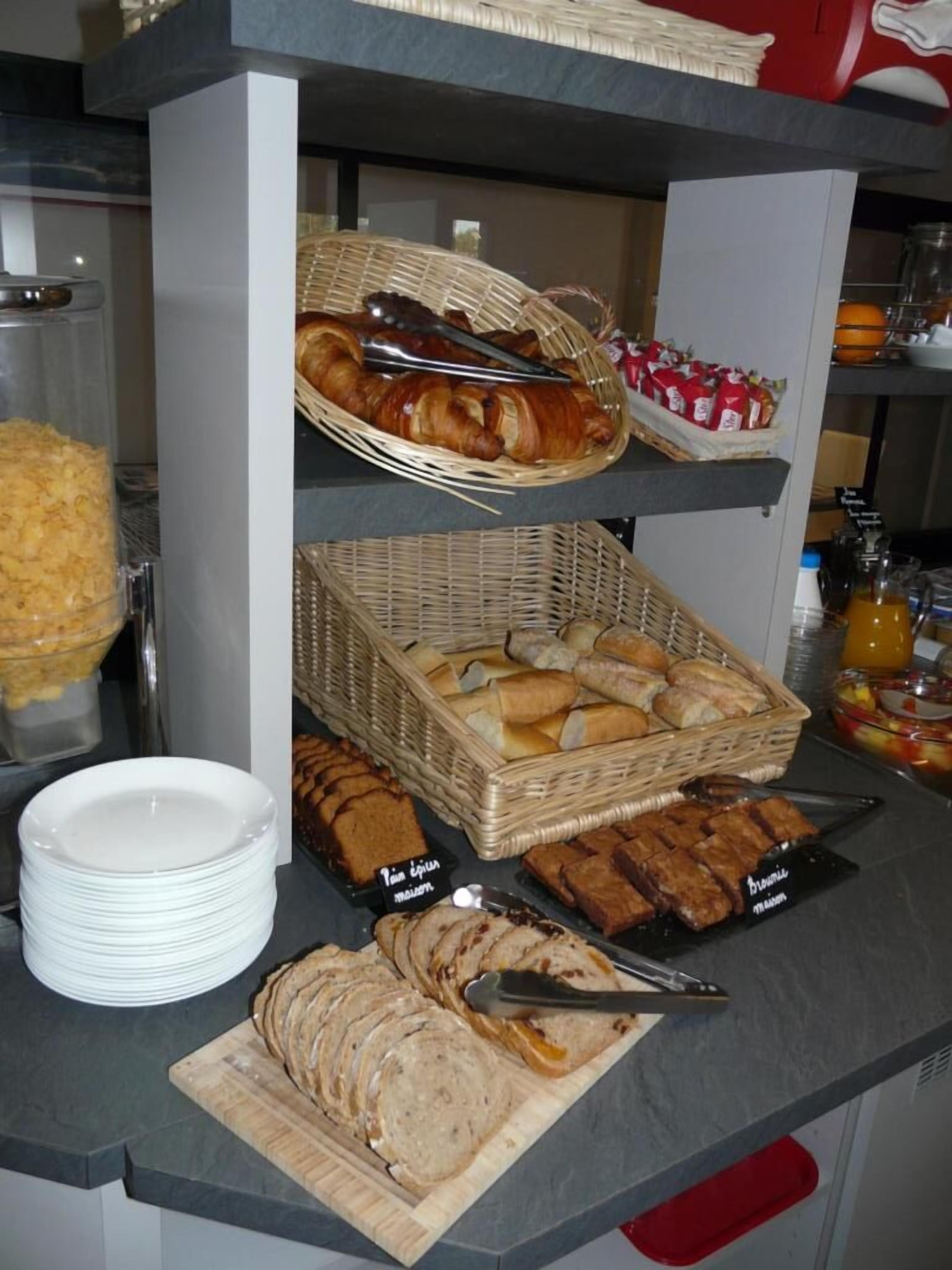 Un comptoir de buffet proposant une variété d’aliments, notamment du pain, des pâtisseries et des viandes en tranches, présentés sur des étagères et dans des paniers.