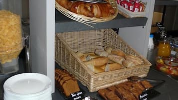 Un comptoir de buffet proposant une variété d’aliments, notamment du pain, des pâtisseries et des viandes en tranches, présentés sur des étagères et dans des paniers.