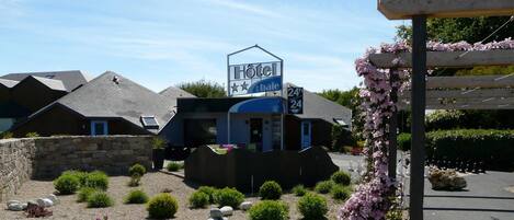 A hotel with a sign indicating it is a bed and breakfast, 24-hour service, and has a small garden area with shrubs and flowers.