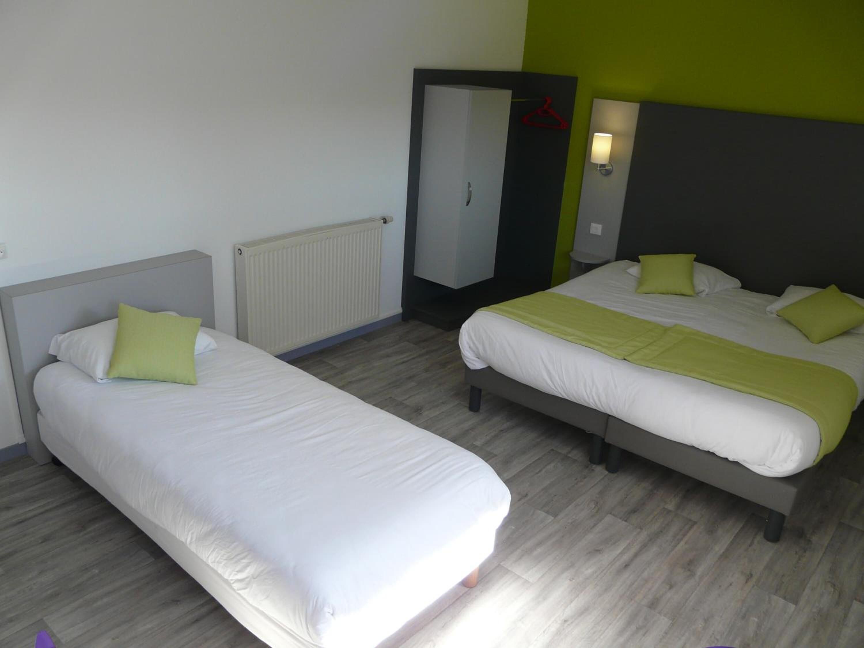 A hotel room with two single beds, a radiator, a wardrobe, and a mirror.