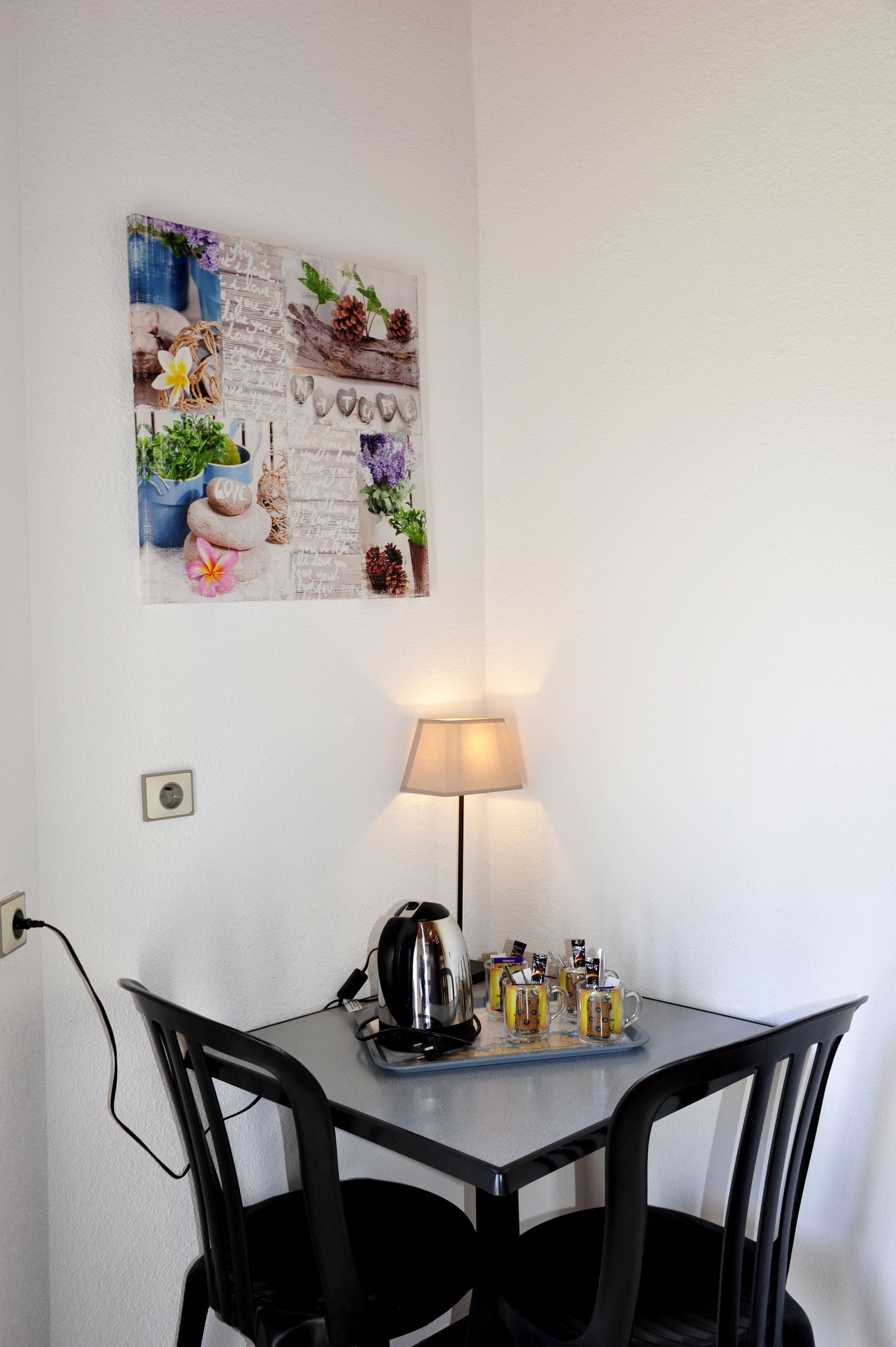 A small dining area with a table, chairs, a lamp, and a wall-mounted artwork.
