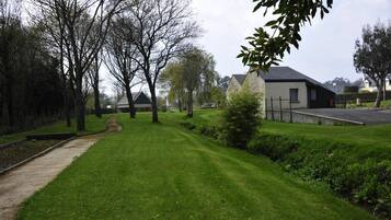 A well-maintained grassy area with a pathway, trees, and a building with a dark roof and white walls.