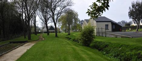 Un área verde bien cuidada con un sendero, árboles y un edificio de techo oscuro y paredes blancas.