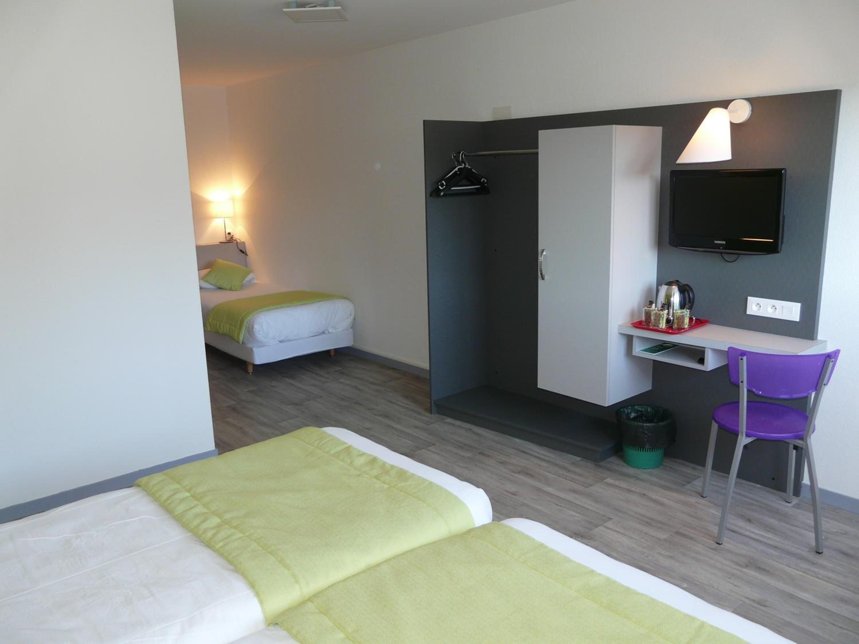 Una habitación de hotel con dos camas, un escritorio con silla, televisión y armario.