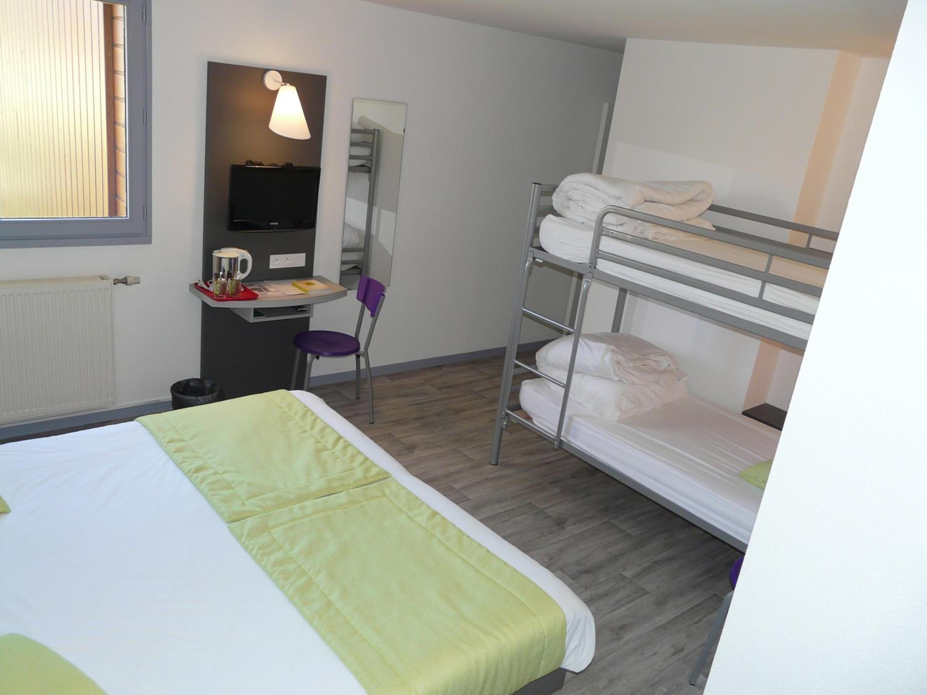 A hotel room with a bunk bed, a desk with a chair, a television, and a window with blinds.
